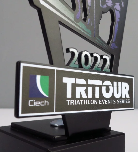 Statuetka Tri Tour wykonana z metalowego panelu wyciętego w ciekawy kształt nawiązujący do trójkąta z kolorowym nadrukiem o motywie triathlonowym - detal 2